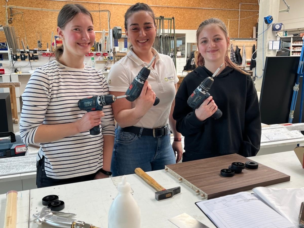 Drei junge Frauen mit Akku-Bohrmaschinen in der Hand in einer Werkstatt.