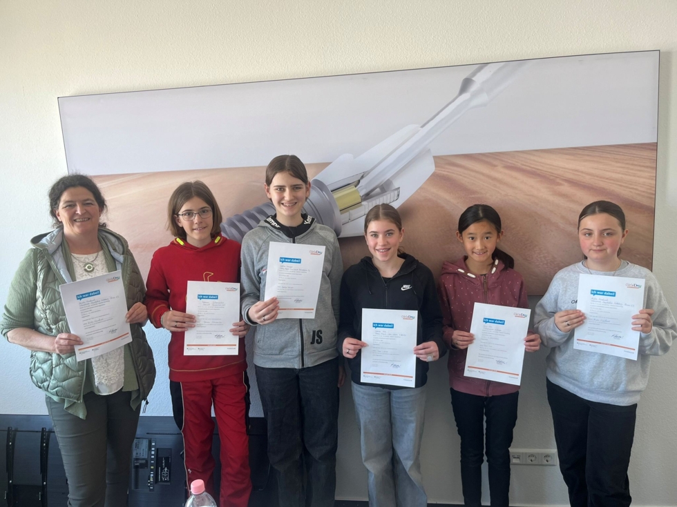 Fünf Girls' Day-Teilnehmerinnen präsentieren stolz ihre Teilnahmebestätigung. Neben ihnen eine Mitarbeiterin