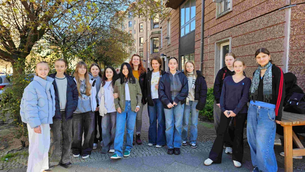 Dreizehn Girls' Day-Teilnehmerinnen stehen draußen vor einem Gebäude, umgeben von Bäumen und Sonnenschein