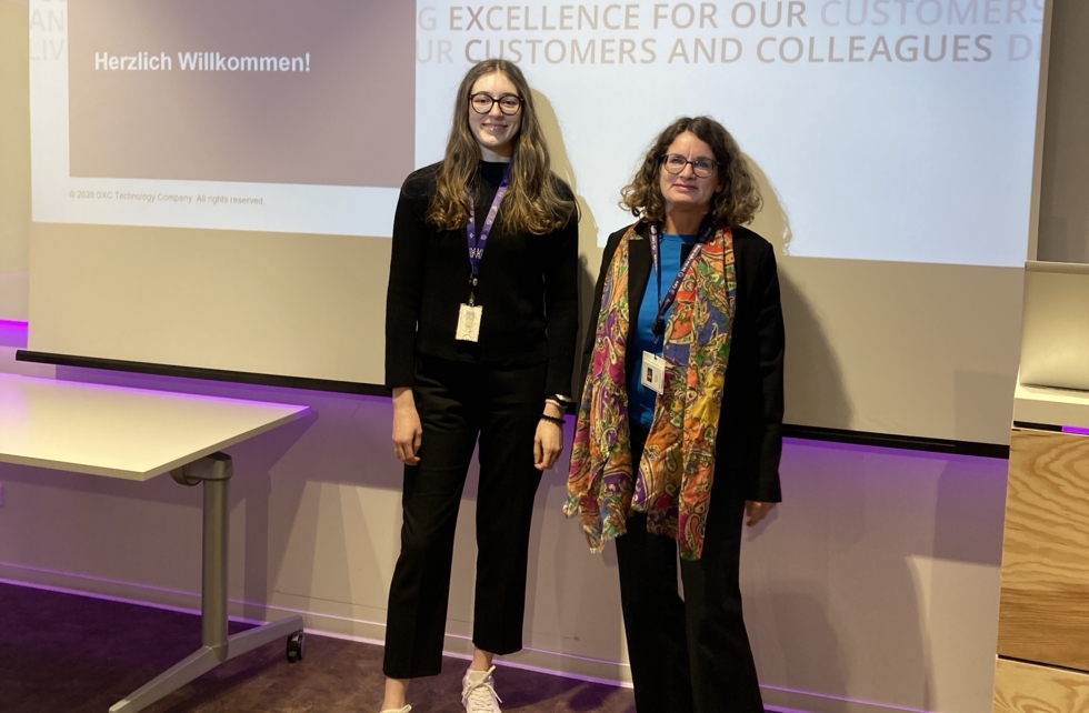 Girls'Day-Teilnehmerin und Mitarbeiterin vor Leinwand mit Schriftzug Herzlich Willkommen