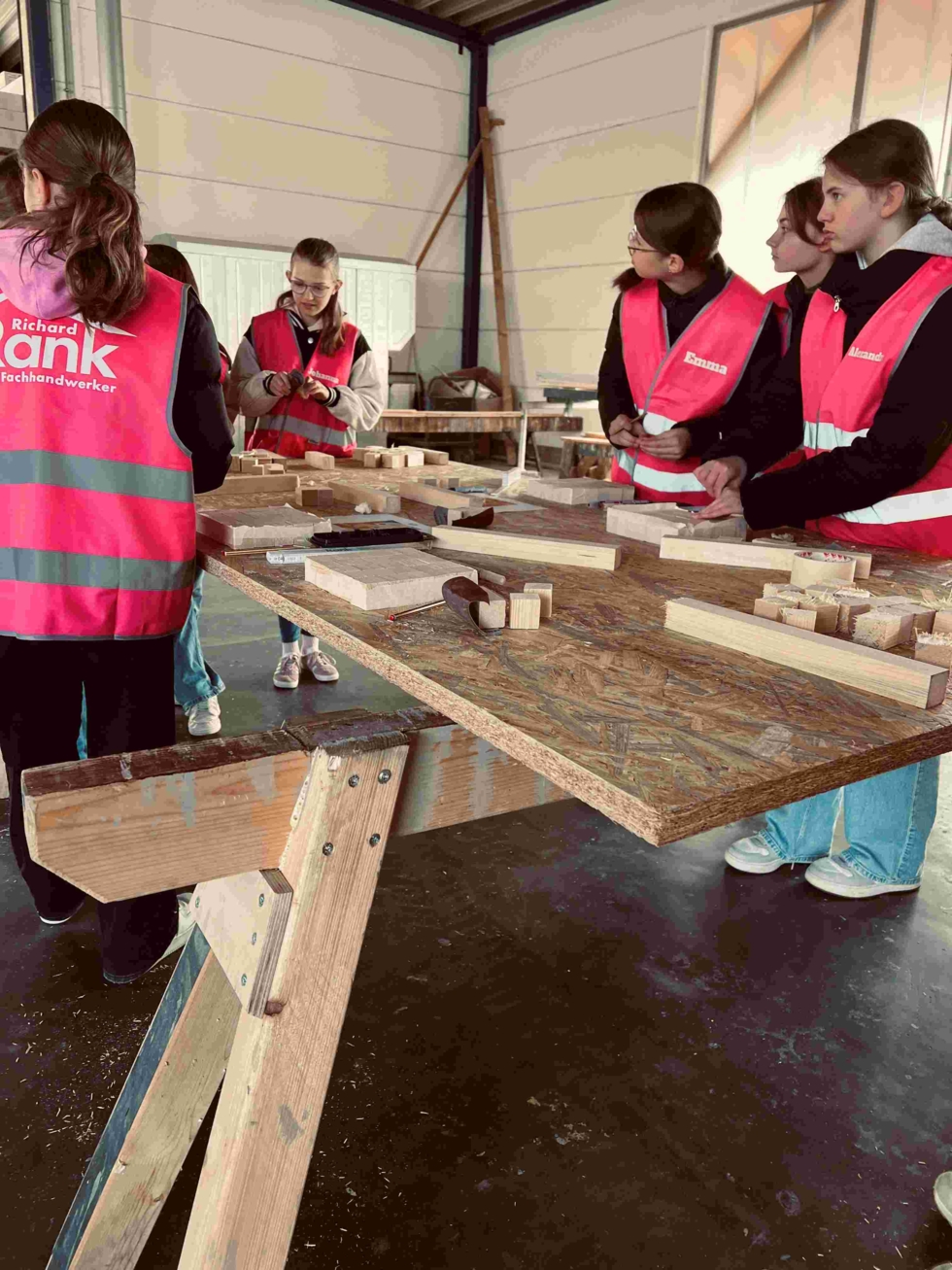 Girls'Day-Teilnehmerinnen mit Warnwesten bauen in Werkstatt mit Holz
