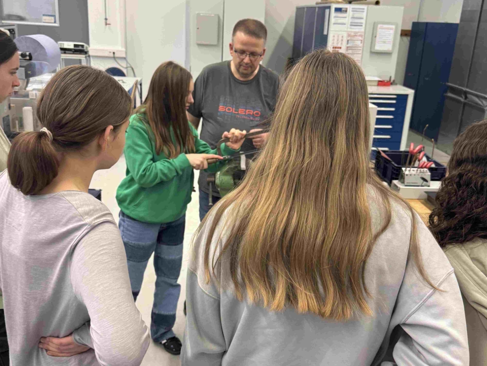 Mädchen bearbeitet ein Metallteil mit einer Säge, andere Mädchen stehen drumherum.