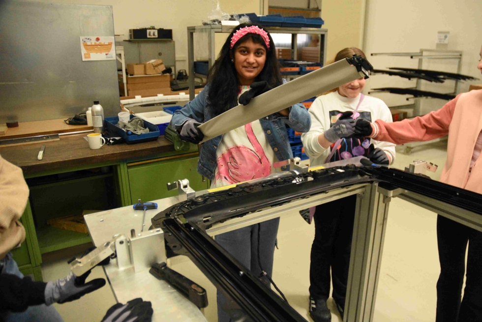 Girls' Day-Teilnehmerin hält ein langes Metallteil in einer Werkstatt mit anderen Girls' Day-Teilnehmerinnen