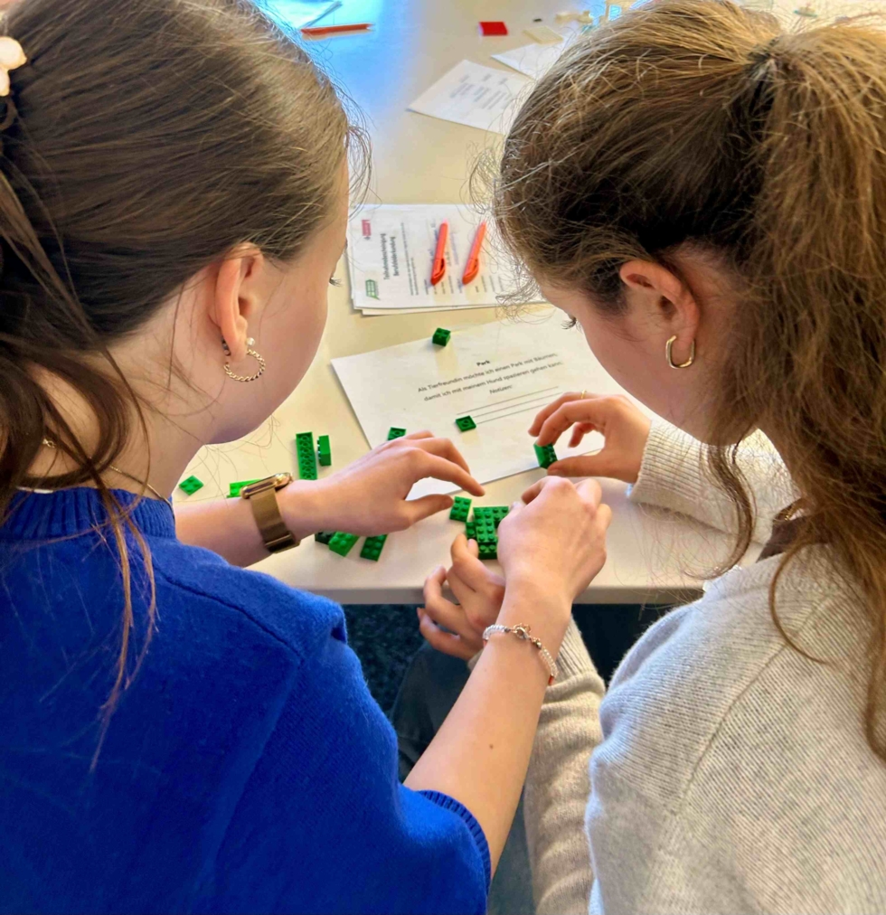 Zwei Girls' Day-Teilnehmerinnen sitzen an einem Tisch und bauen gemeinsam mit grünen Bausteinen aus Plastik