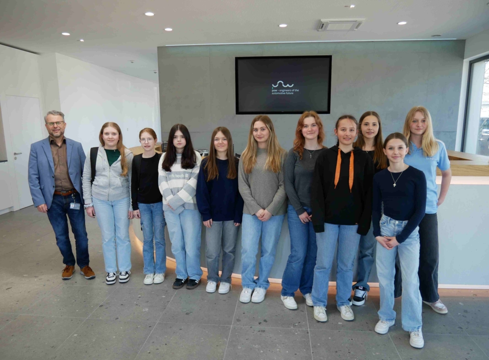 Neun Girls' Day-Teilnehmerinnen und zwei Mitarbeitende stehen nebeneinander in einem modernen Raum