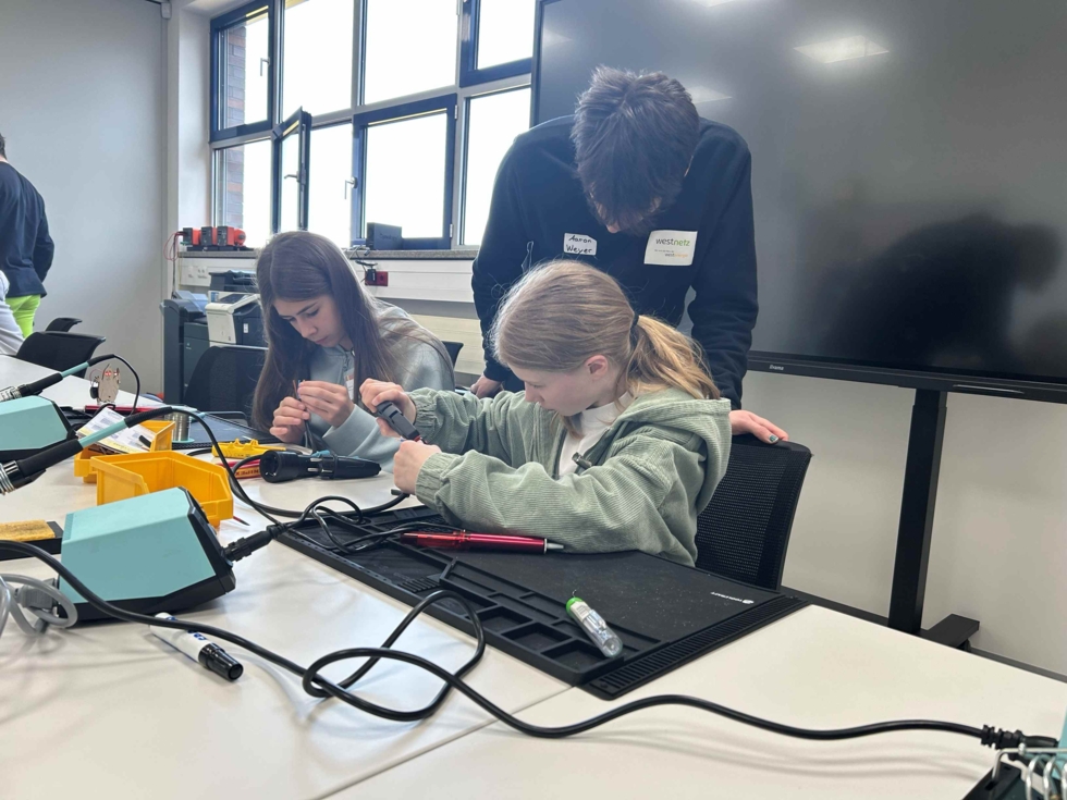 Girls' Day Teilnehmerinnen sitzen an einem Tisch und fertigen ein elektronisches Gespenst an unter Anleitung der Mitarbeiter