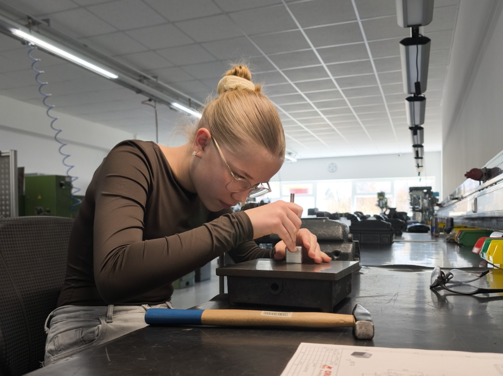 Eine junge Frau mit Brille arbeitet konzentriert an einem Würfel aus Metall.