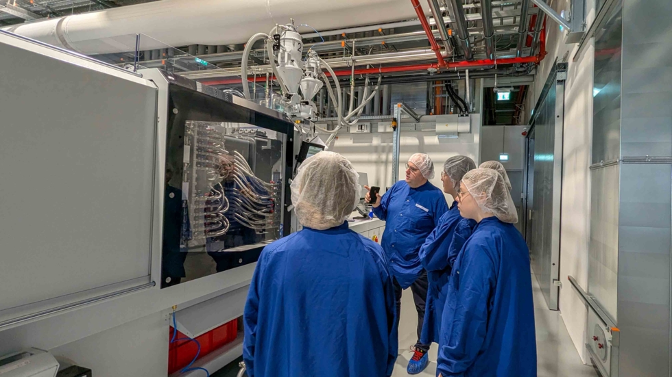 Girls'Day-Teilnehmerinnen mit Schutzanzügen schauen Maschine an