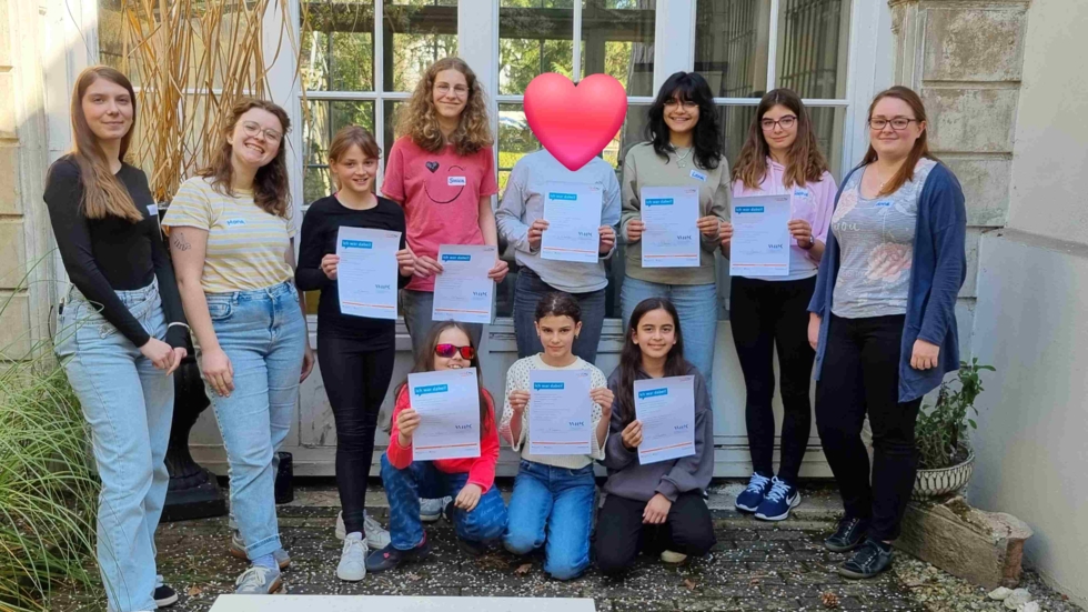 Gruppe von neun Personen, darunter Mitarbeiter und Girls' Day-Teilnehmerinnen, die Teilnahmebescheinigungen in einem Innenhof halten